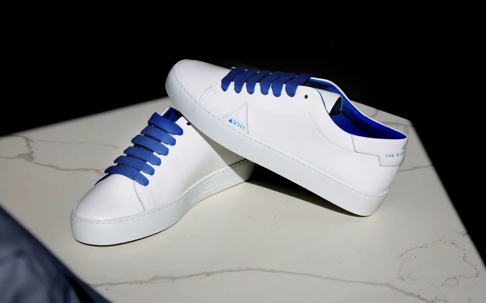 White leather sneakers with blue laces on a marble surface